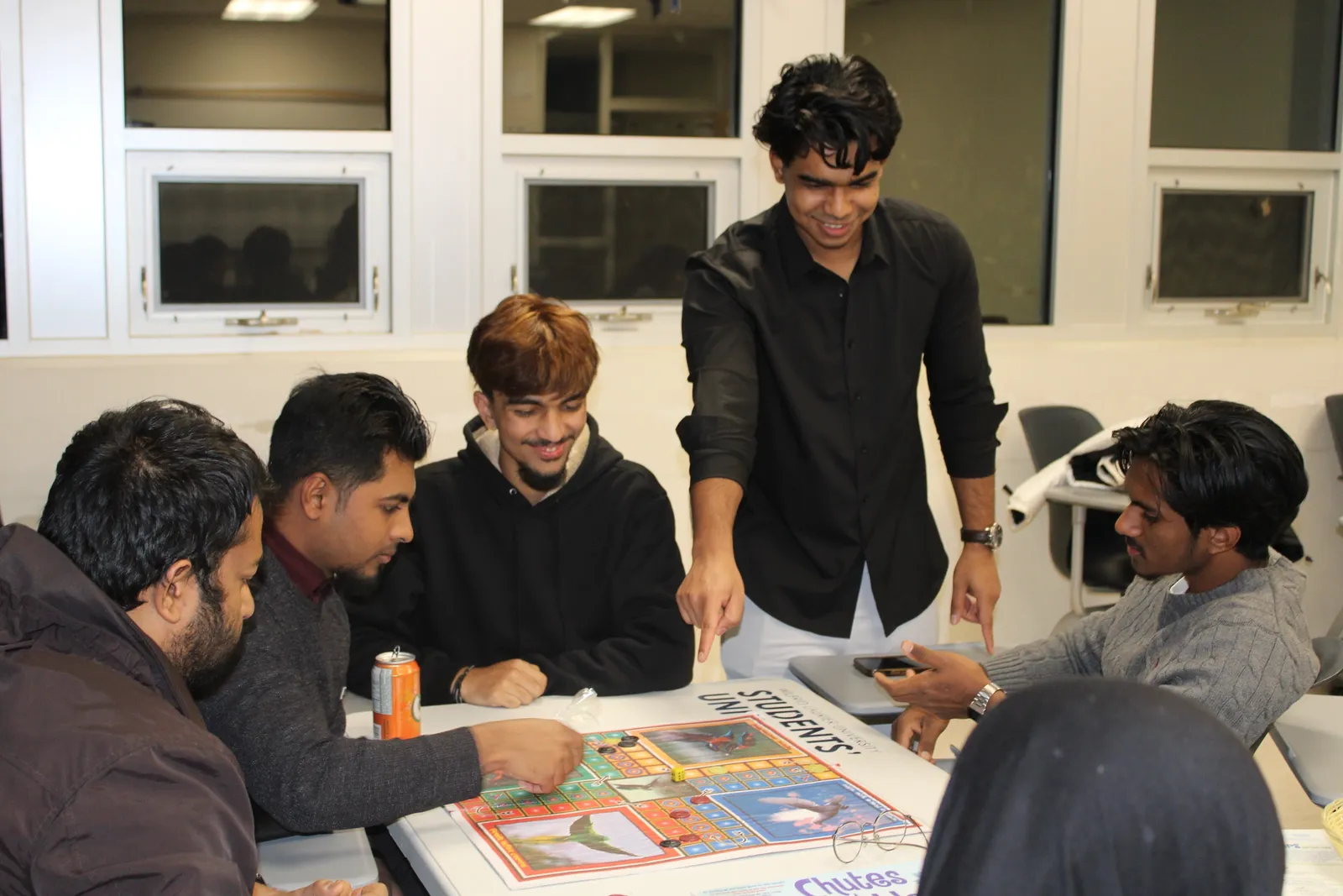 Students playing a board game at Khela Hobe while one points at the board and laughs.